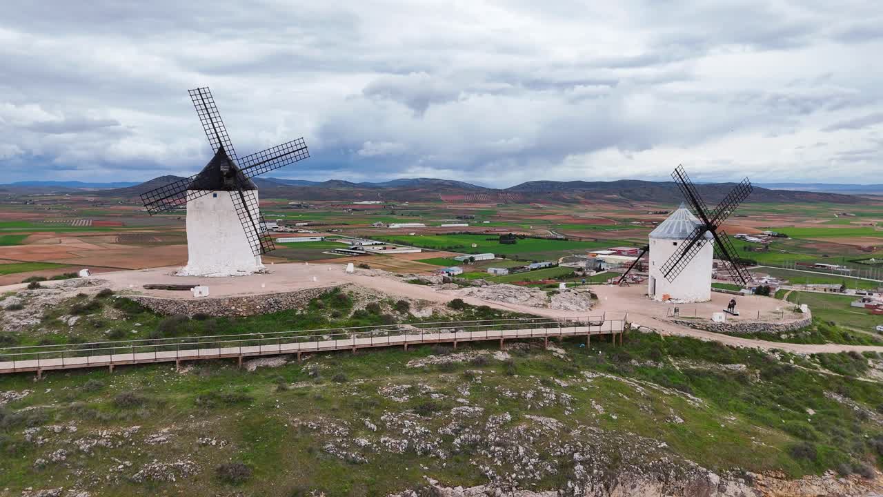 Slow-motion drone view of two Consuegra windmills on cloudy day