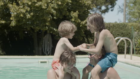 two boys sitting on father and brother's necks and having fun in the swimming pool