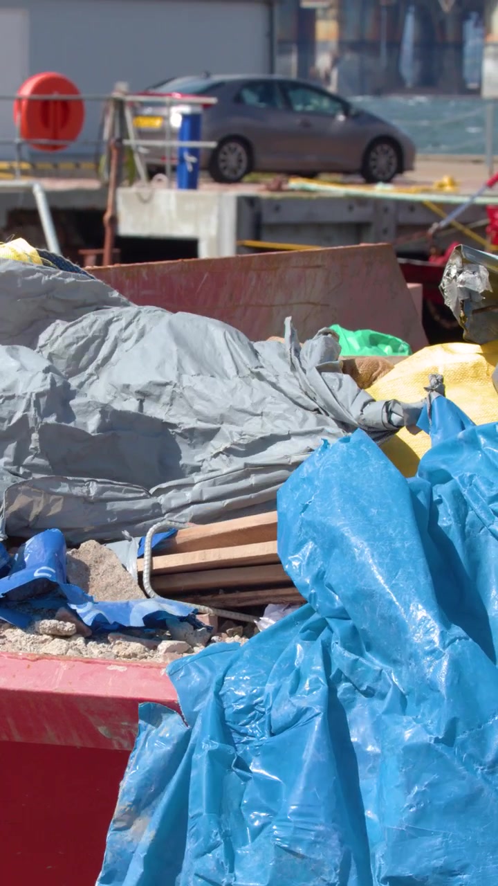 Raffiche di vento soffiano teli di plastica e spazzatura in un cassone aperto al porto di Cromarty, alla luce del giorno.
