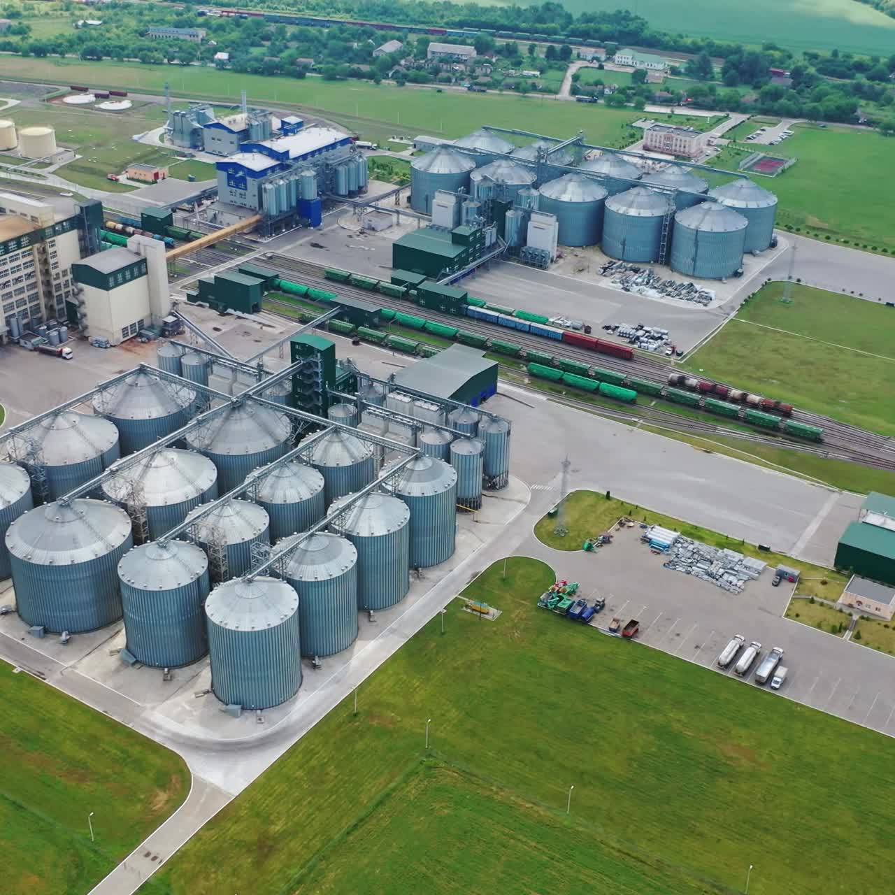 Agricultural land and grain silo. Steel grain silos elevators storage among green nature. Agriculture Industry. Aerial video.
