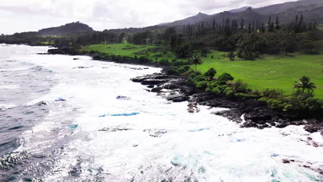 Panorámica-Aérea-En-Rápido-Movimiento-Alrededor-De-Un-Video-De-Ondas-Azules-Translúcidas-Rompiendo-Sobre-La-Pared-Rocosa-Afilada-Y-Dentada-En-Hawaii-En-Un-Día-Caluroso-Y-Húmedo-Durante-Un-Viaje-De-Senderismo-Costero-En-La-Isla.