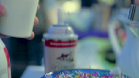delicious sprinkles are scooped from a bowl in slow motion and poured onto the whip cream of hot chocolate