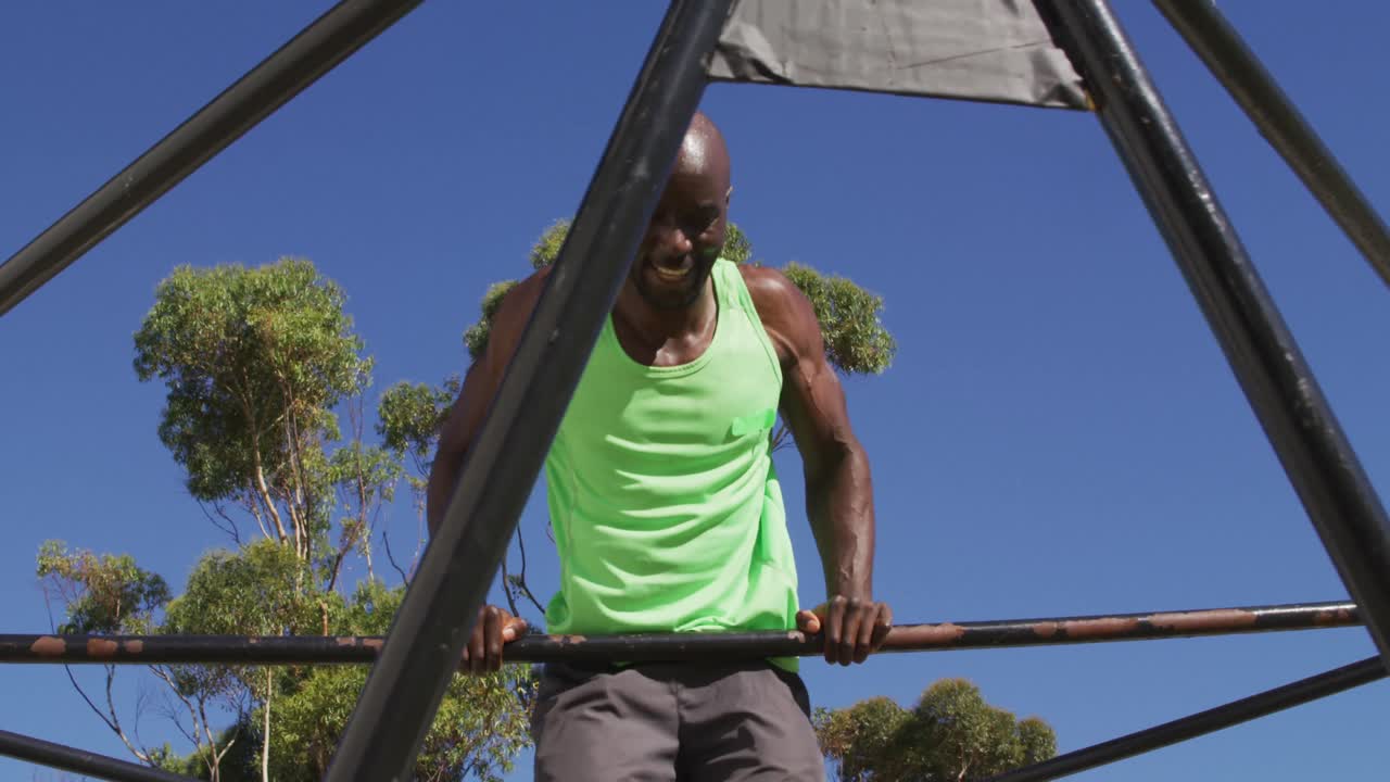 hombre afroamericano en forma haciendo ejercicio afuera, haciendo flexiones en un marco de escalada