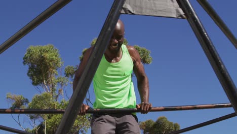 Fit african american man exercising outside, doing push ups on a climbing frame