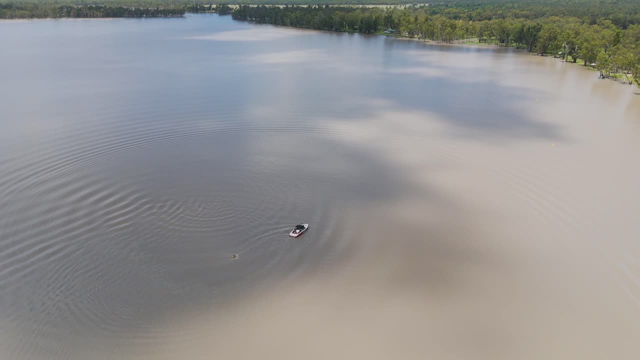 드론이 평온한 호수에서 스키 선수를 견인하는 보트를 포착합니다.