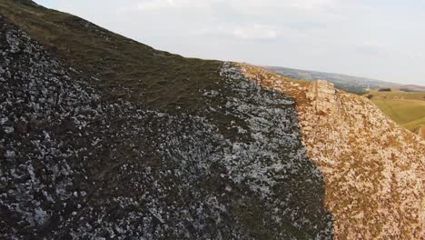 Drone-flies-along-limestone-cliff-edge-down-valley-of-Winnats-Pass-England-at-sunset