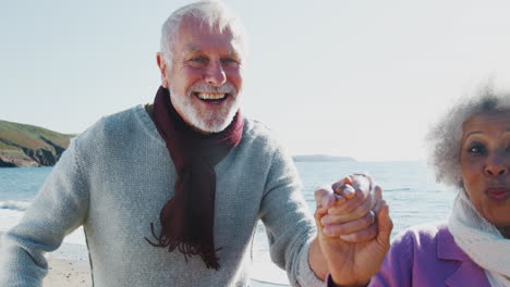 Portrait-Of-Active-Senior-Couple-Running-Along-Beach-By-Waves-Holding-Hands