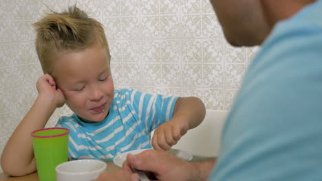 Hijo-Hablando-Con-Padre-Y-Comiendo-Usando-Una-Cuchara-Y-Sonriendo