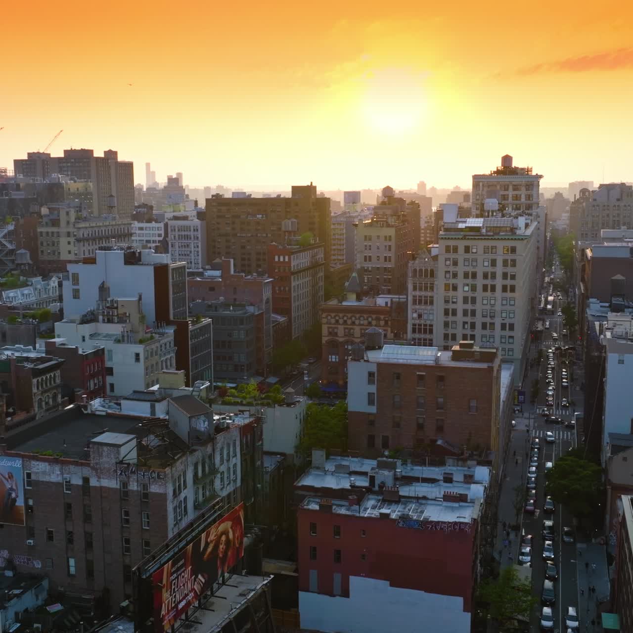 Setting sun over the multi-storied buildings of New York. Drone rising over a busy street of metropolis. Orange sky backdrop
