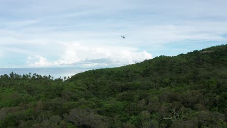 Helicopter-with-cargo-hanging-from-cable-flying-towards-helipad-on-remote-island