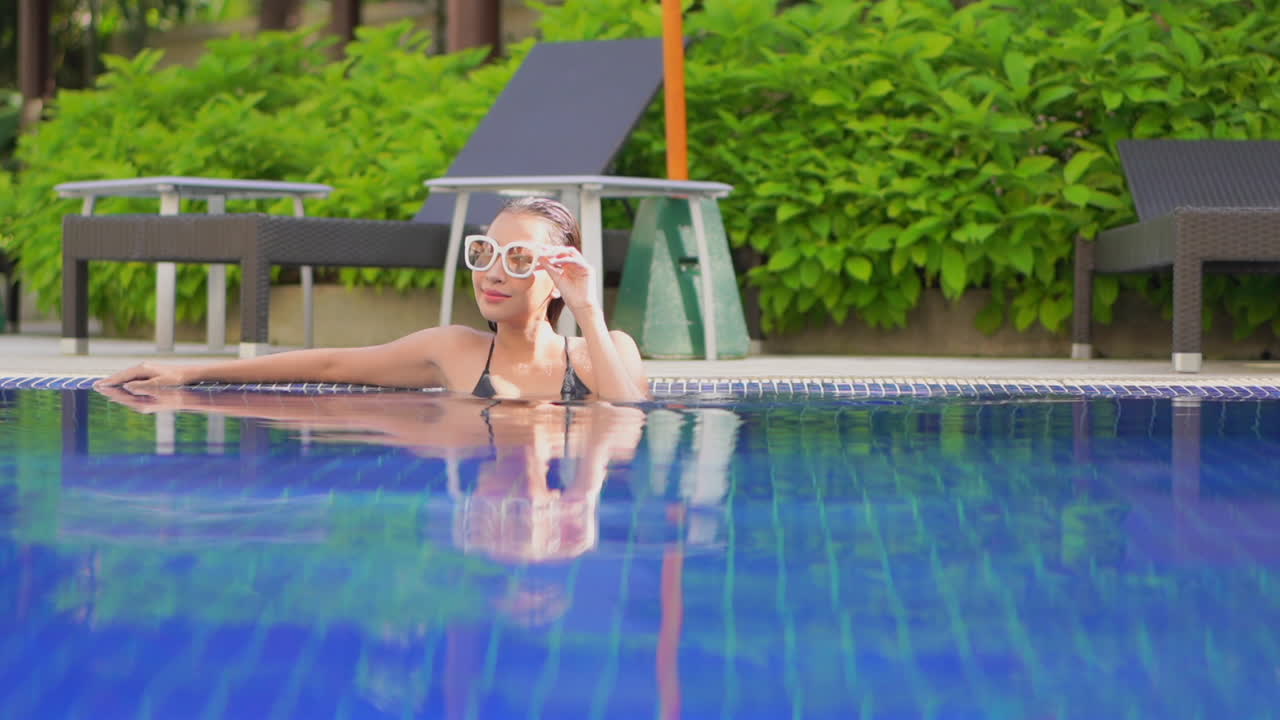 una mujer joven y bonita que acaba de nadar reclama su espacio extendiendo los brazos a lo largo del borde de la piscina de un centro turístico