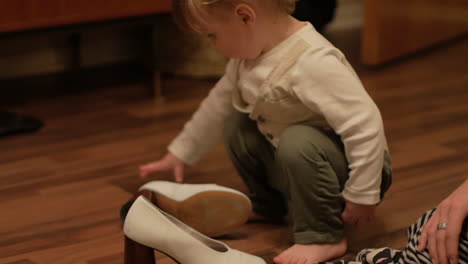 Un-Lindo-Niño-Gordito-Arreglando-Unos-Zapatos-Blancos-De-Tacón-En-El-Piso-De-Madera---Primer-Plano