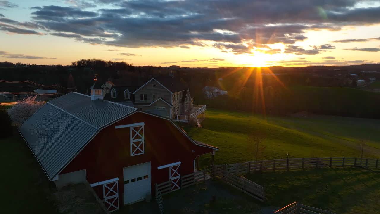 Landlig gårdscene med lade og hus i en grøn engdal. Smuk solnedgang og dramatisk himmel, afsløring fra luften.