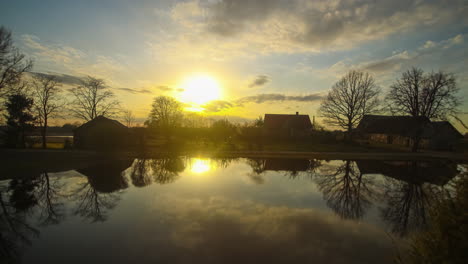 Timelapse-of-setting-sun-and-dramatic-clouds-in-sky-reflecting-in-lake-by-homes
