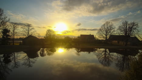 timelapse of setting sun and dramatic clouds in sky reflecting in lake by homes