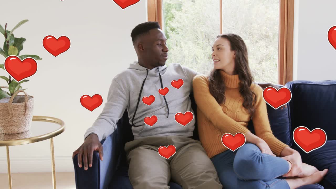 Woman touching his shoulder, couple sitting navy sofa showing affection, romance hearts overlaying