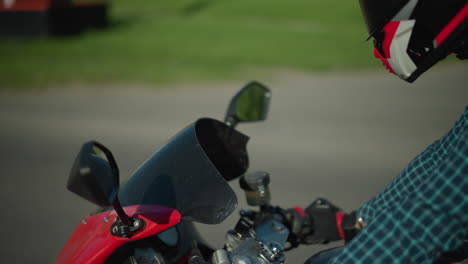 a close-up view of a female motorcyclist riding a red power bike, wearing a checkered shirt and canvas shoes, helmet on, a parked car is faintly visible in the background