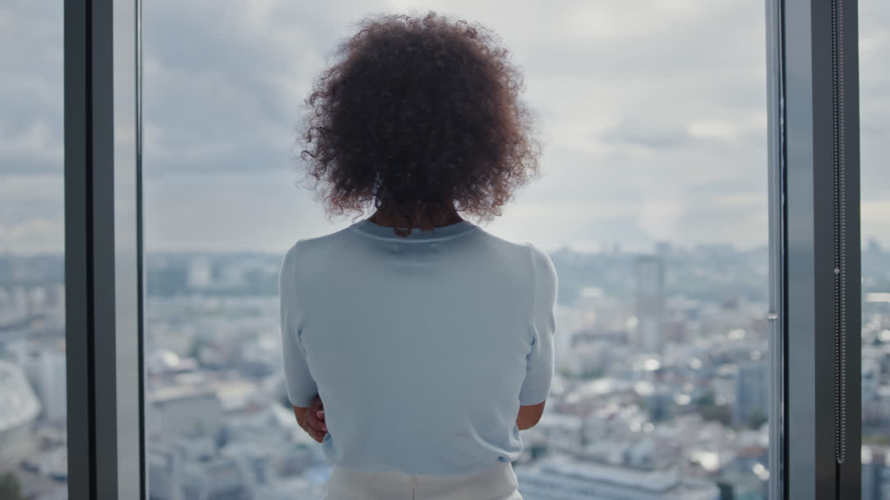 Businesswoman standing at window in office. Entrepreneur enjoying city view