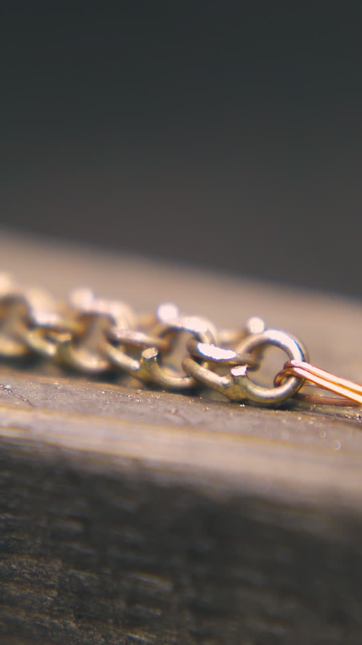 CU: skilled goldsmith polishes shining gold chain with rasp on wooden gutter on blurred background in workshop extreme closeup