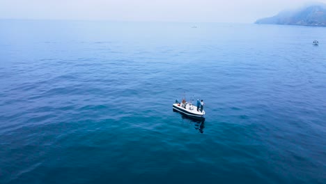 aerial orbit a lone fishing boat in the blue waters near coronado islands, mexico, with vast open ocean surrounding, fishermen stand with reflection below