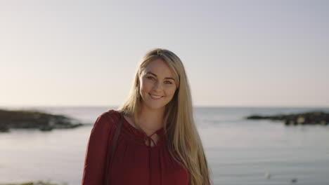 portrait of lovely young blonde woman smiling confident on beach removes sunglasses posing to camera in calm seaside beach background