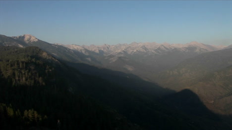 A-person-stands-near-a-cliff-and-looks-out-at-the-forest-covered-mountains