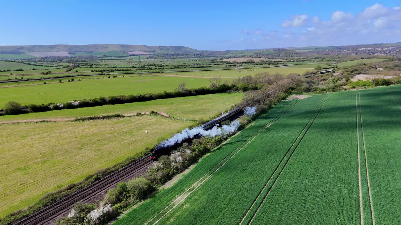 Breathtaking aerial drone footage of the Sussex Belle steam train, billowing steam as it travels through the scenic English Sussex countryside. Perfect for heritage and travel visuals.