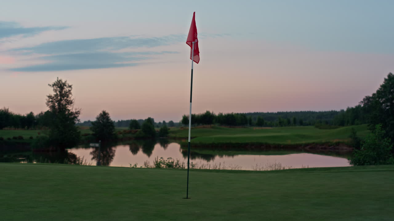 Golf course red flag in golfing hole. Flagstaff on empty green course sunset.
