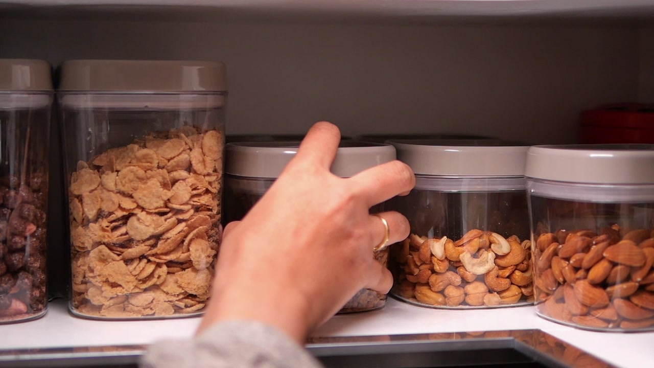 Hand Taking Granola Container from Organized Pantry Shelf
