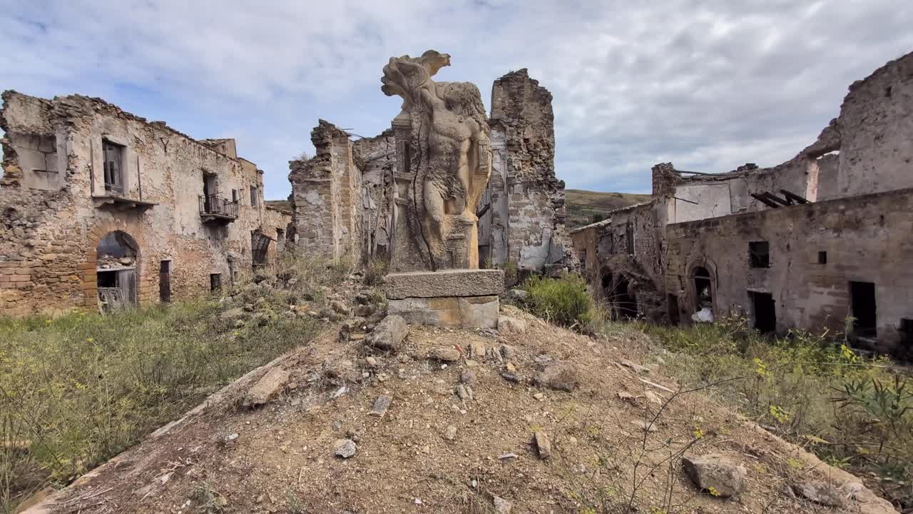 Slow pan of a damaged statue in the main square of Poggioreale ghost town, Sicily, Italy. Earthquake ruins and crumbling buildings frame this haunting abandoned site