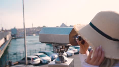 cámara lenta: hermosa joven mira a través de binoculares de turismo con vista a la torre de galata y al distrito de eminonu en estambul, turquía