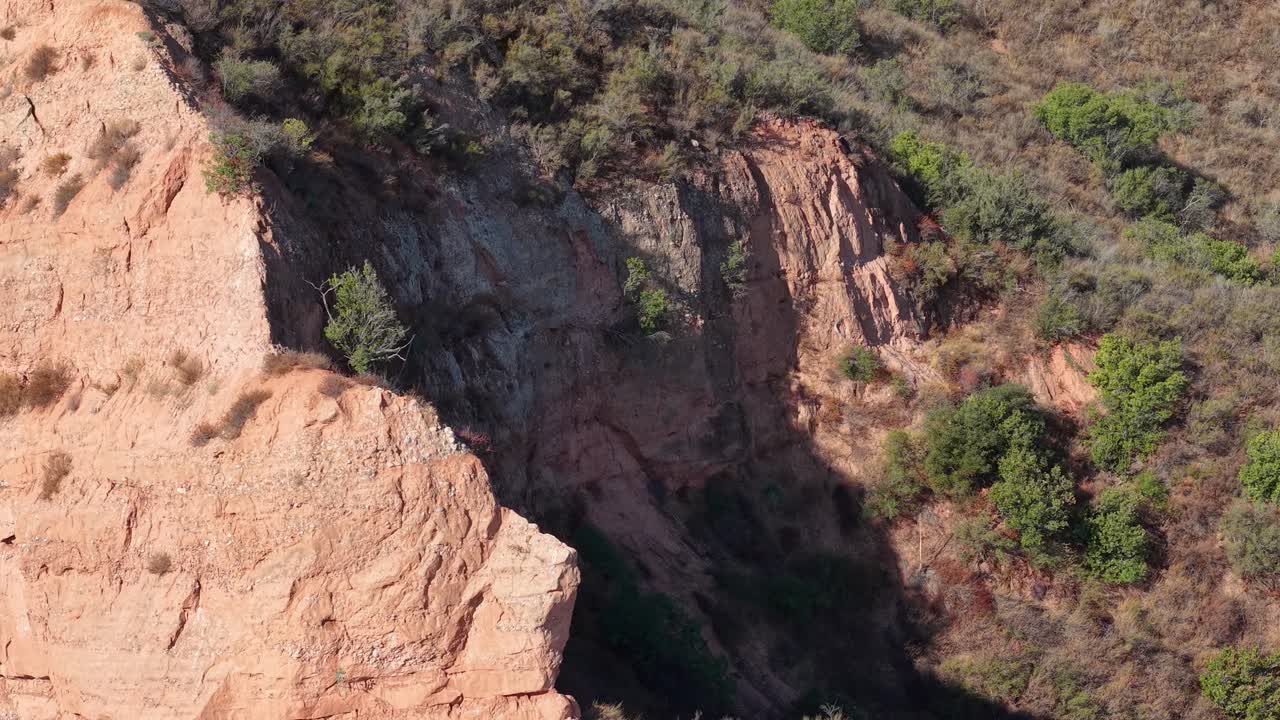 Close-up aerial shot of steep canyon walls in Black Star Canyon, showcasing textured rock faces and sparse vegetation in golden light