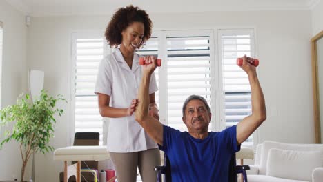 Mixed-race-female-physiotherapist-helping-senior-man-exercise-using-dumbbells