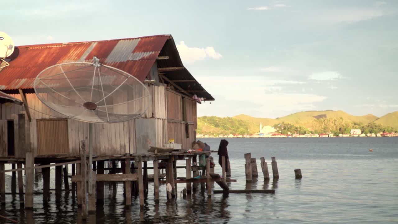 Stilted houses in the water's edge with green hills in the background