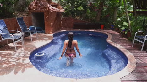 long hair woman in knit bikini walks slo mo into small resort pool