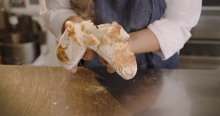 Seeing loaves on cooling rack female baker in apron selecting splitting, smelling loaf for quality