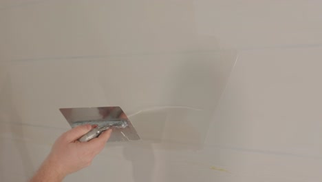 man plastering the walls with finishing putty in room with putty spatula