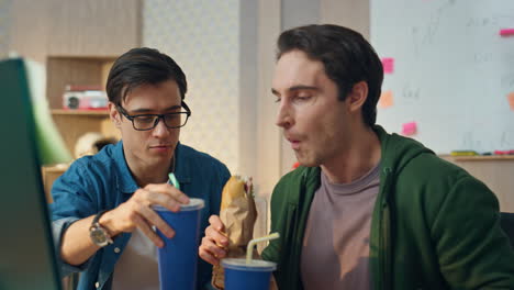 happy colleagues eating lunch looking monitor close up. freelancers discussing