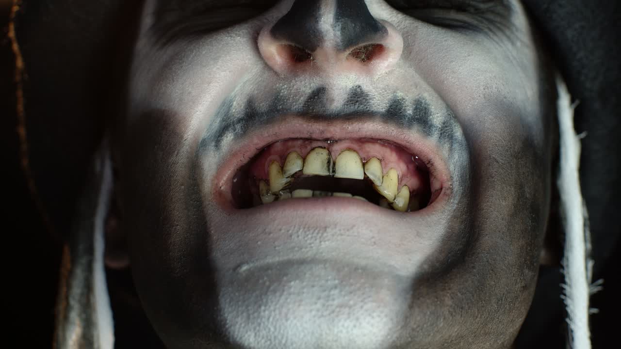 골격 메이크업을 한 남자가 겁을 주려고 입을 열고 더러운 검은 이빨과 혀를 보여줍니다.