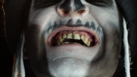 man with skeleton makeup trying to scare, opening his mouth and showing dirty black teeth and tongue