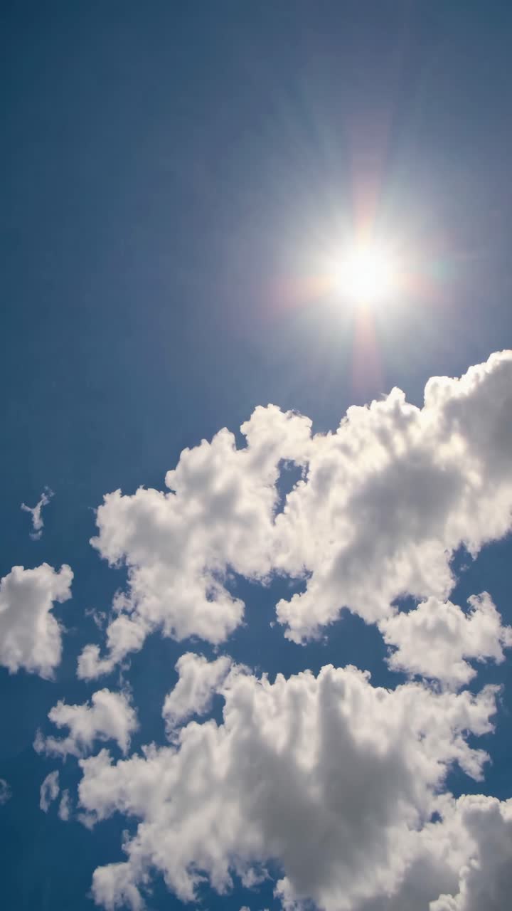Un video riprende un'inquadratura dal basso di un sole splendente e nuvole soffici contro un cielo azzurro limpido