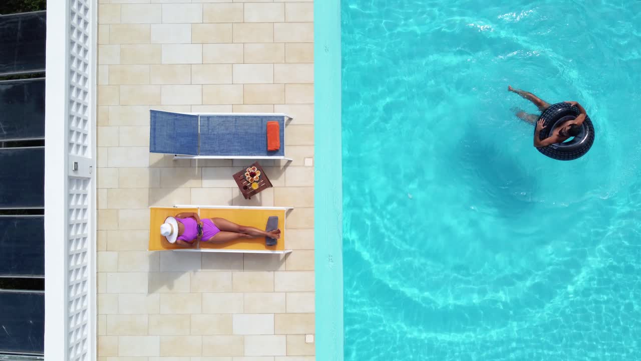 Draufsicht auf ein Paar, das den Pool eines Resorts während der Sommerferien genießt.