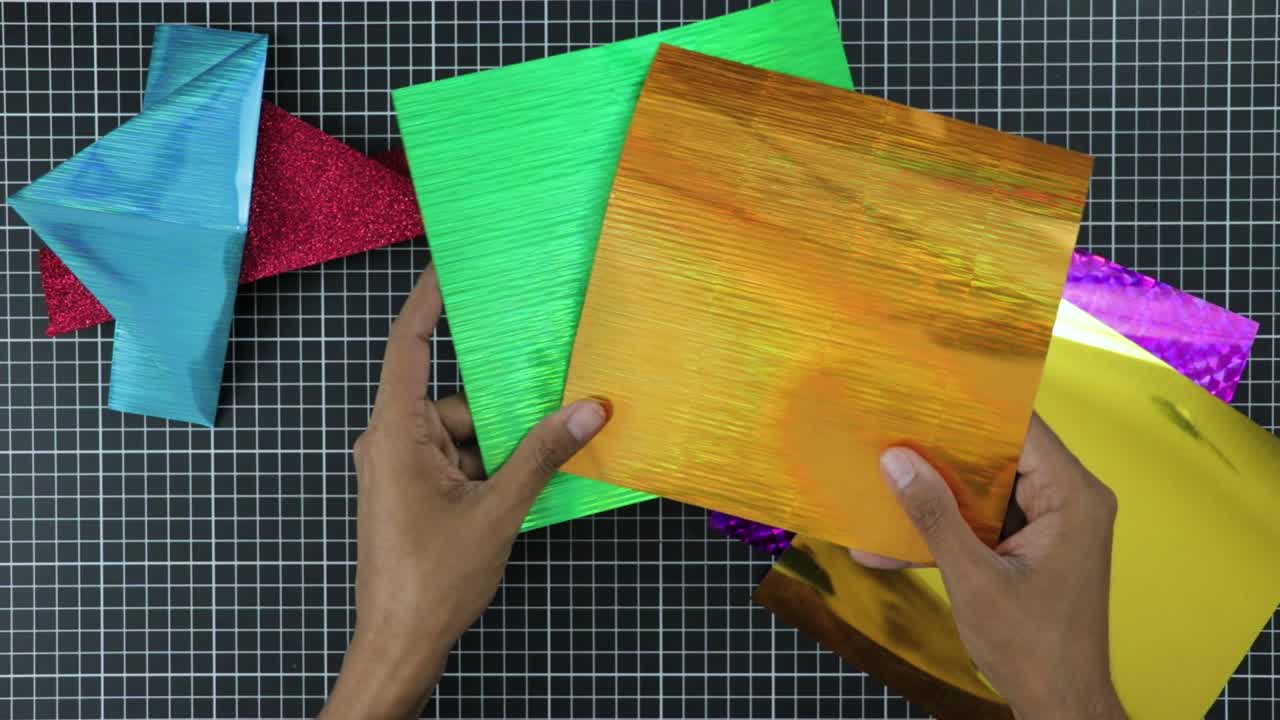 manos que muestran papel de material de pvc metalizado muy colorido para artesanías
