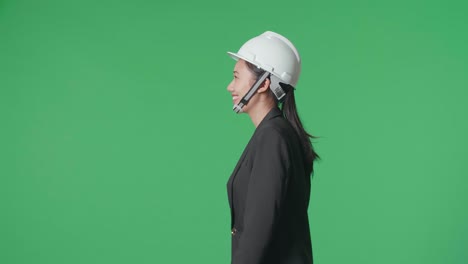 side view of smiling asian female engineer looking around and shaking her head while walking in the green screen studio