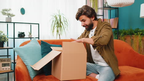 Happy-arabian-man-shopper-unpacking-cardboard-box-delivery-parcel-online-shopping-purchase-at-home