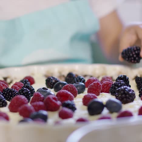 little girl placing a blackberry on a pie