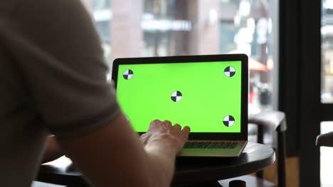man using laptop computer with green screen in restaurant