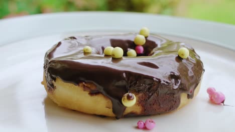 Yellow-pink-sprinkles-falling-on-chocolate-cream-donut-close-up