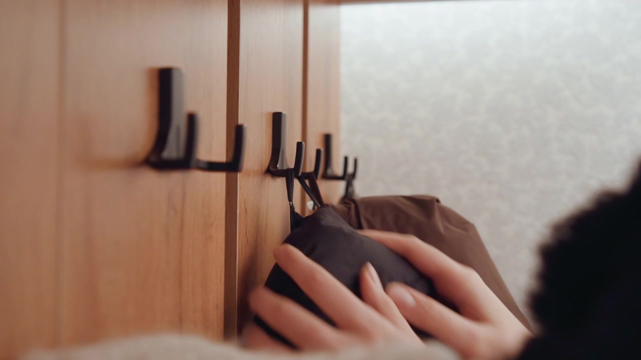 Mano che appende un cappotto. Un pendolare urbano sistema la giacca. Un caldo piumino viene appeso a un gancio di legno. La luminosa luce del mattino illumina una scena ordinata nell'ingresso mentre la giacca viene appesa con un movimento rapido.