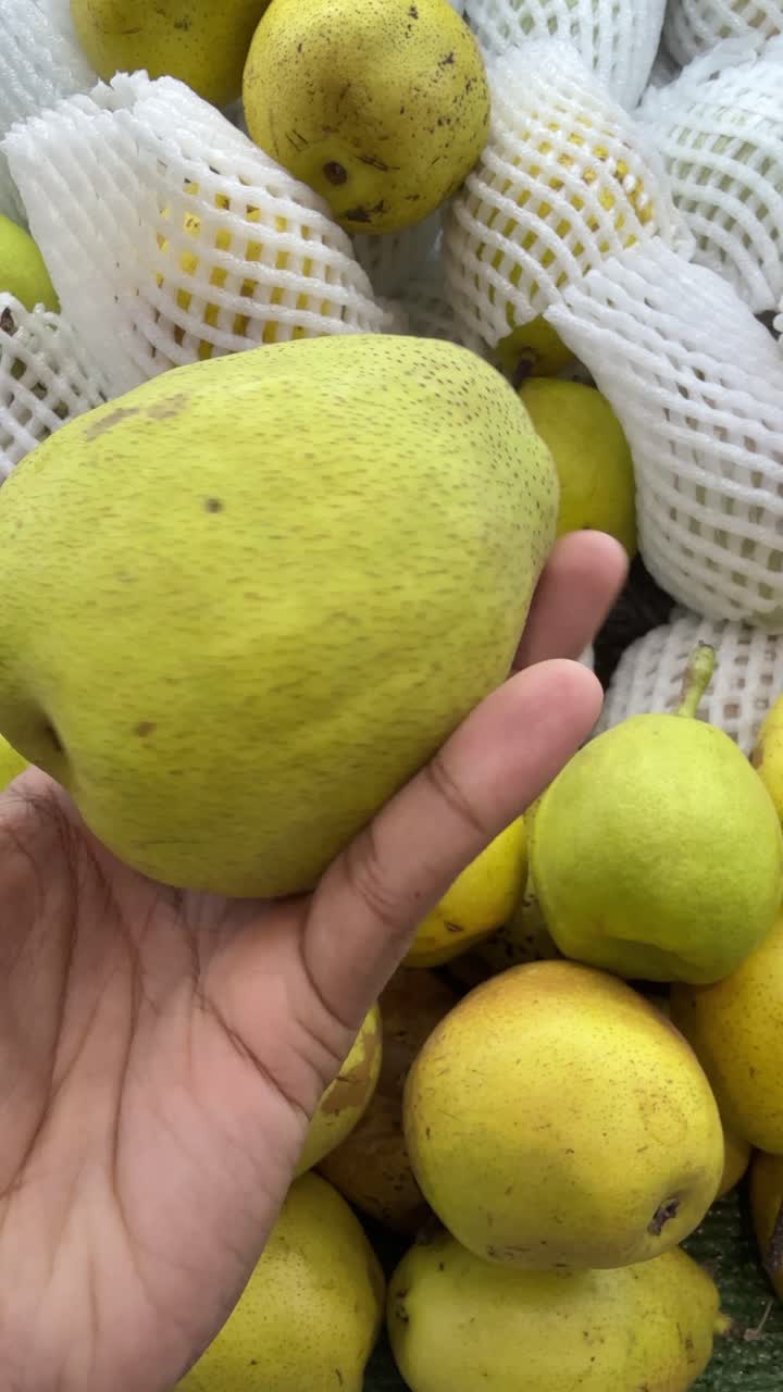 Mano che tiene e ruota una pera verde fresca in un mercato